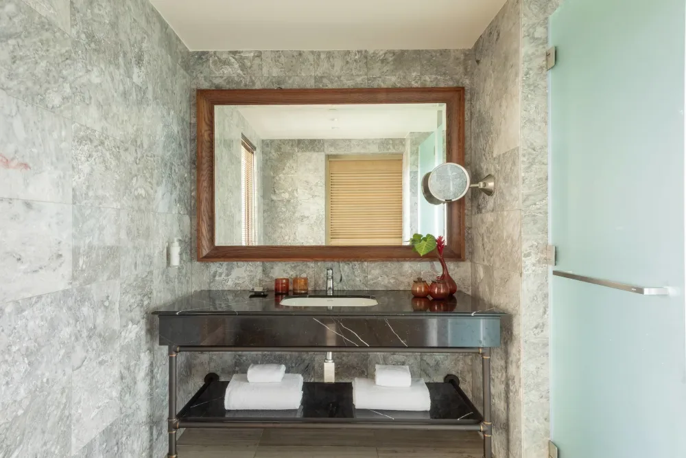 The stone tiled bathroom with a dark marble vanity and wood framed mirror