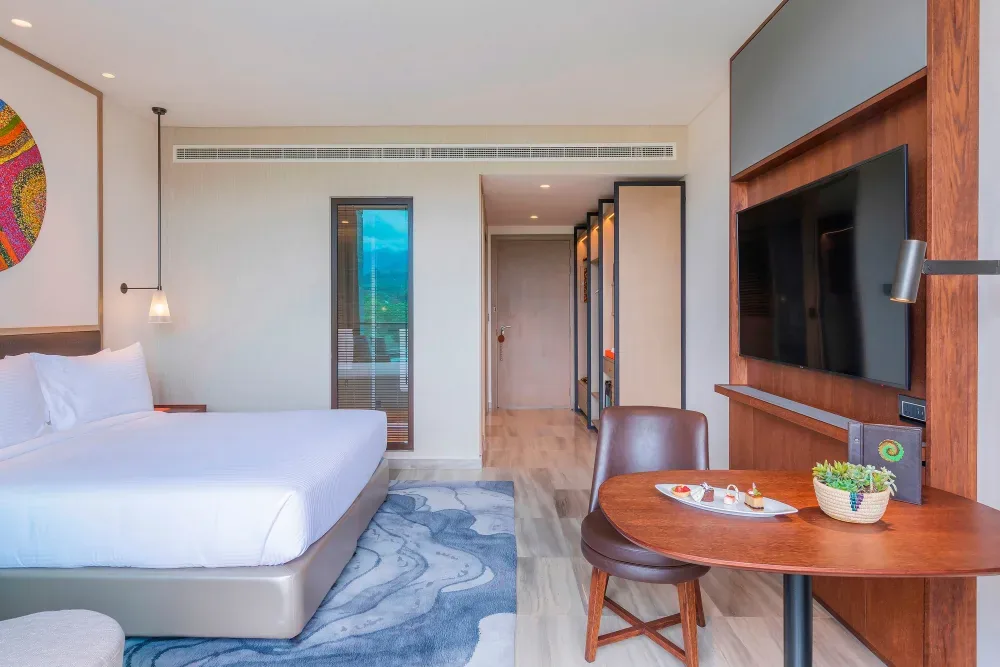 The Deluxe Room with a table and chair by the TV and a window to the garden