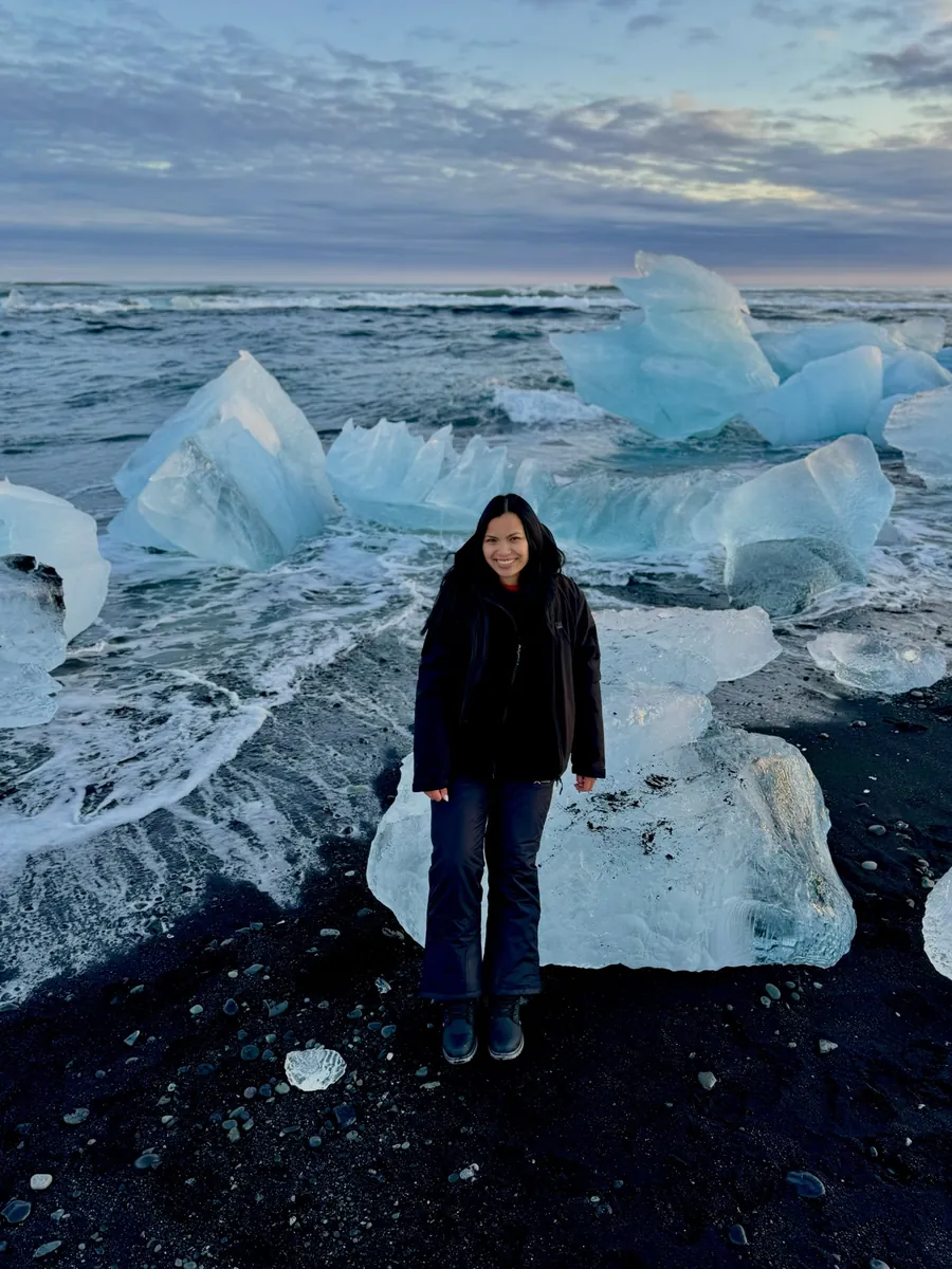 Jea Breshears standing among blocks of glacier ice on the black sand of Diamond Beach, Iceland