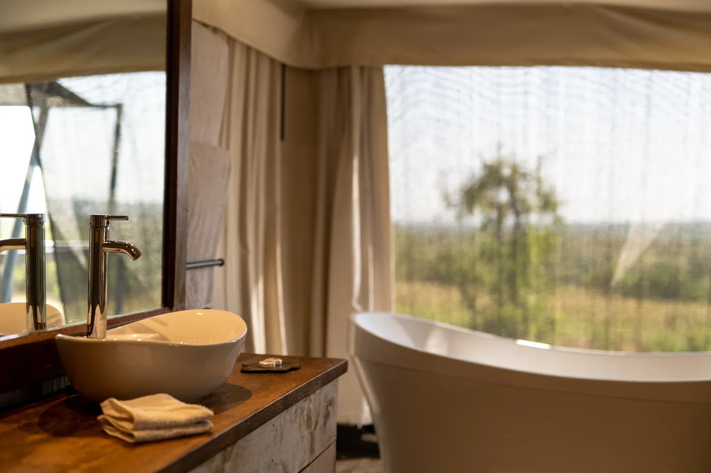 A freestanding bathtub beside the tent window looking out at the Serengeti bush