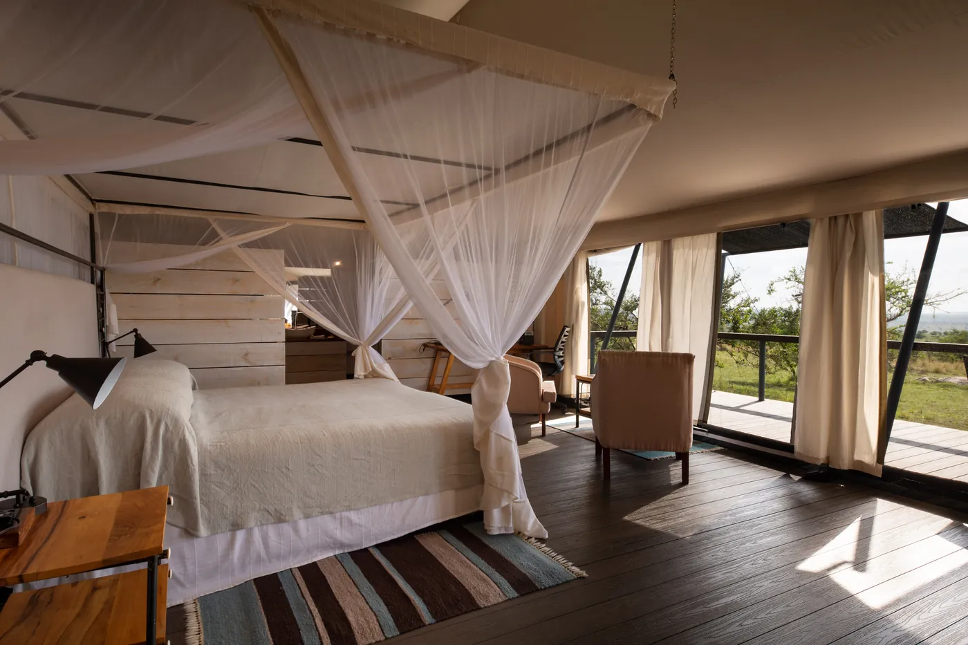 A tent at Mara Mara Tented Lodge with a canopy bed, wooden floors and doors open to the deck
