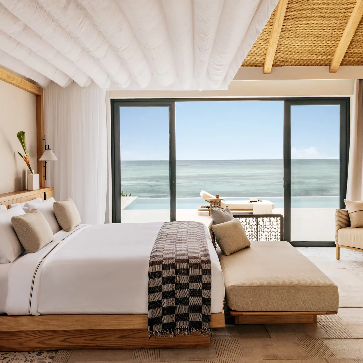 The bedroom of a one bedroom Ocean Villa at Meli&aacute; Zanzibar, opening onto a private infinity pool and the Indian Ocean
