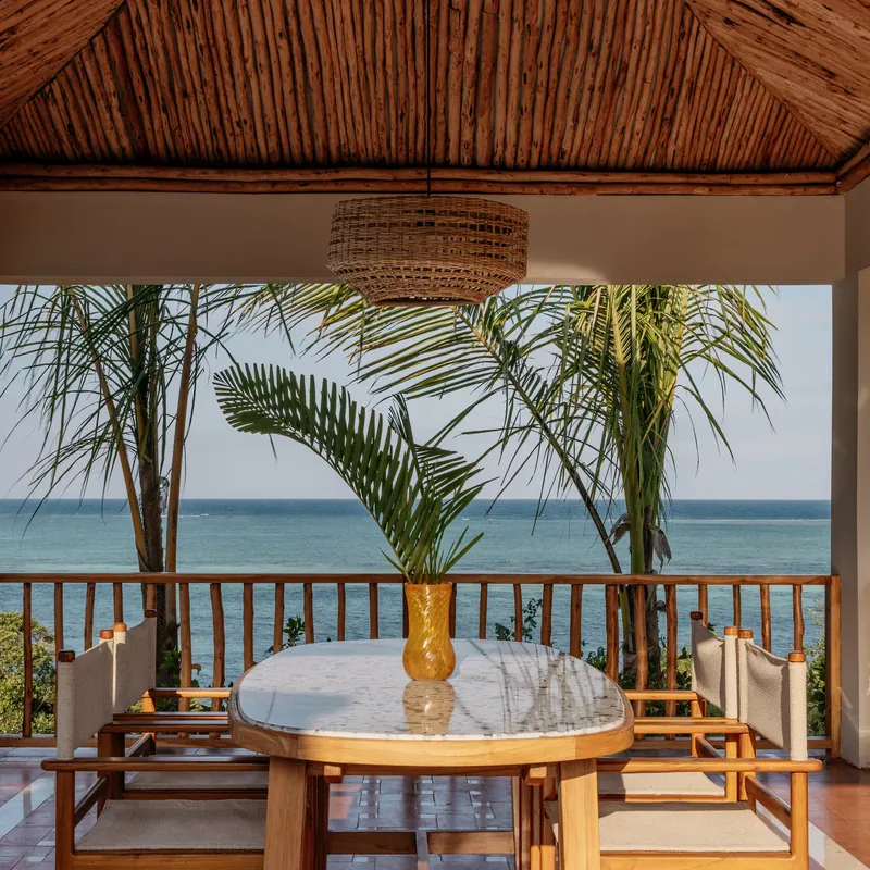 A covered dining table on the villa terrace, framed by palms and the ocean