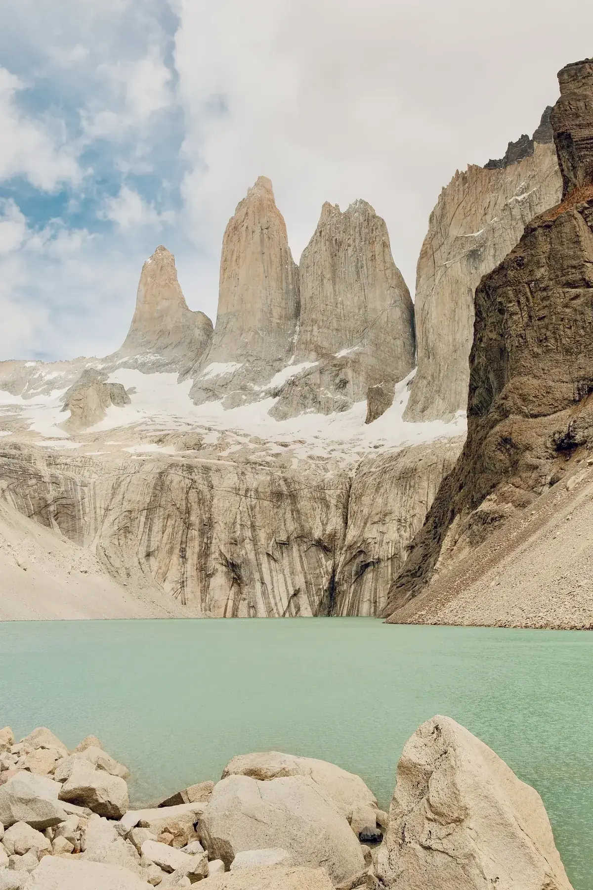 The three granite towers of Torres del Paine rising above scree slopes under a cloudy sky